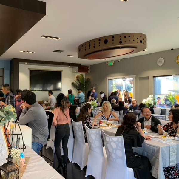 A busy Mikayla's Cafe dining room with many patrons seated at tables and standing near a bar.