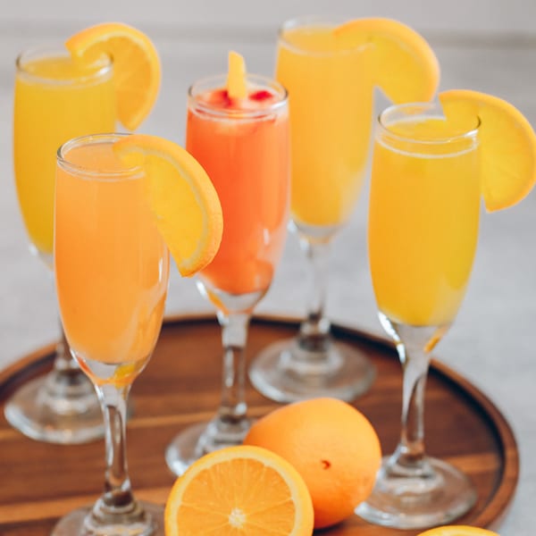 Mikayla's Cafe mimosas in champagne flutes, garnished with orange slices, on a wooden tray.