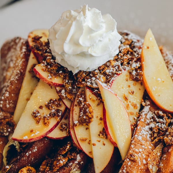 Mikayla's Cafe French toast topped with whipped cream, apple slices, granola, and powdered sugar.