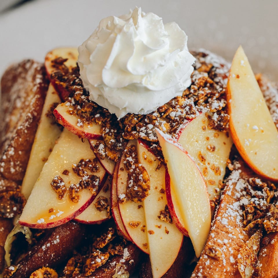 Mikayla's Cafe French toast topped with whipped cream, apple slices, granola, and powdered sugar.