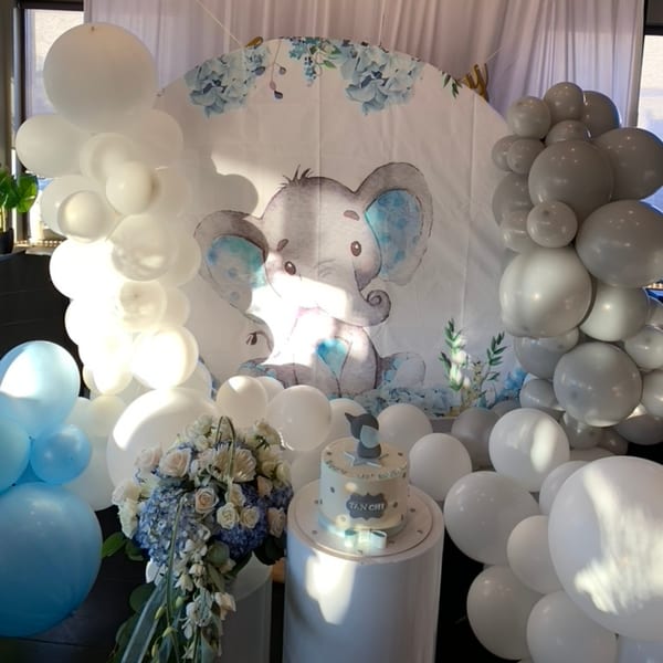 Baby shower decorations with blue and white balloons, a cake, and an elephant backdrop.