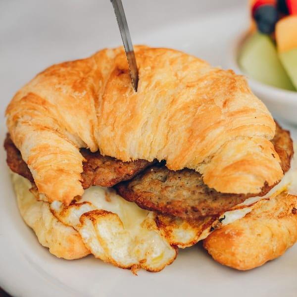 A croissant breakfast sandwich with sausage, egg, and cheese, with a knife cutting into it.