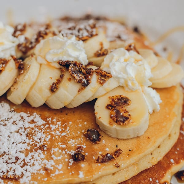 Mikayla's Cafe pancakes topped with sliced bananas, whipped cream, granola, and powdered sugar.