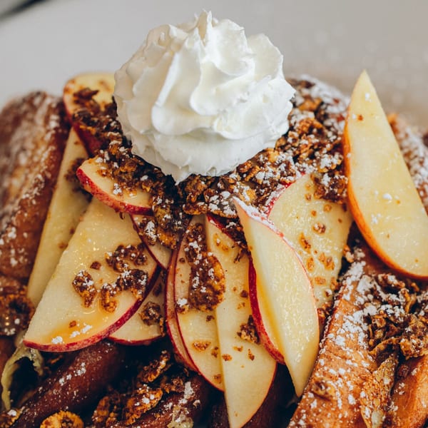 Mikayla's Cafe French toast topped with whipped cream, apple slices, granola, and powdered sugar.