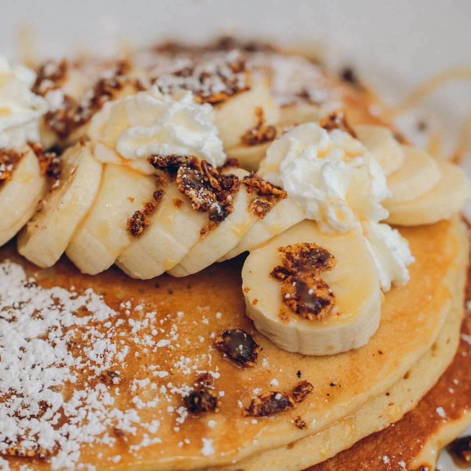 Mikayla's Cafe banana pancakes with whipped cream, granola, powdered sugar, and syrup.
